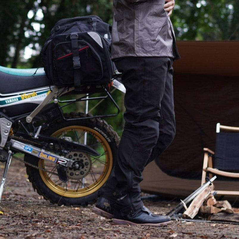 Person in a raincoat standing next to a motorcycle with a forest background